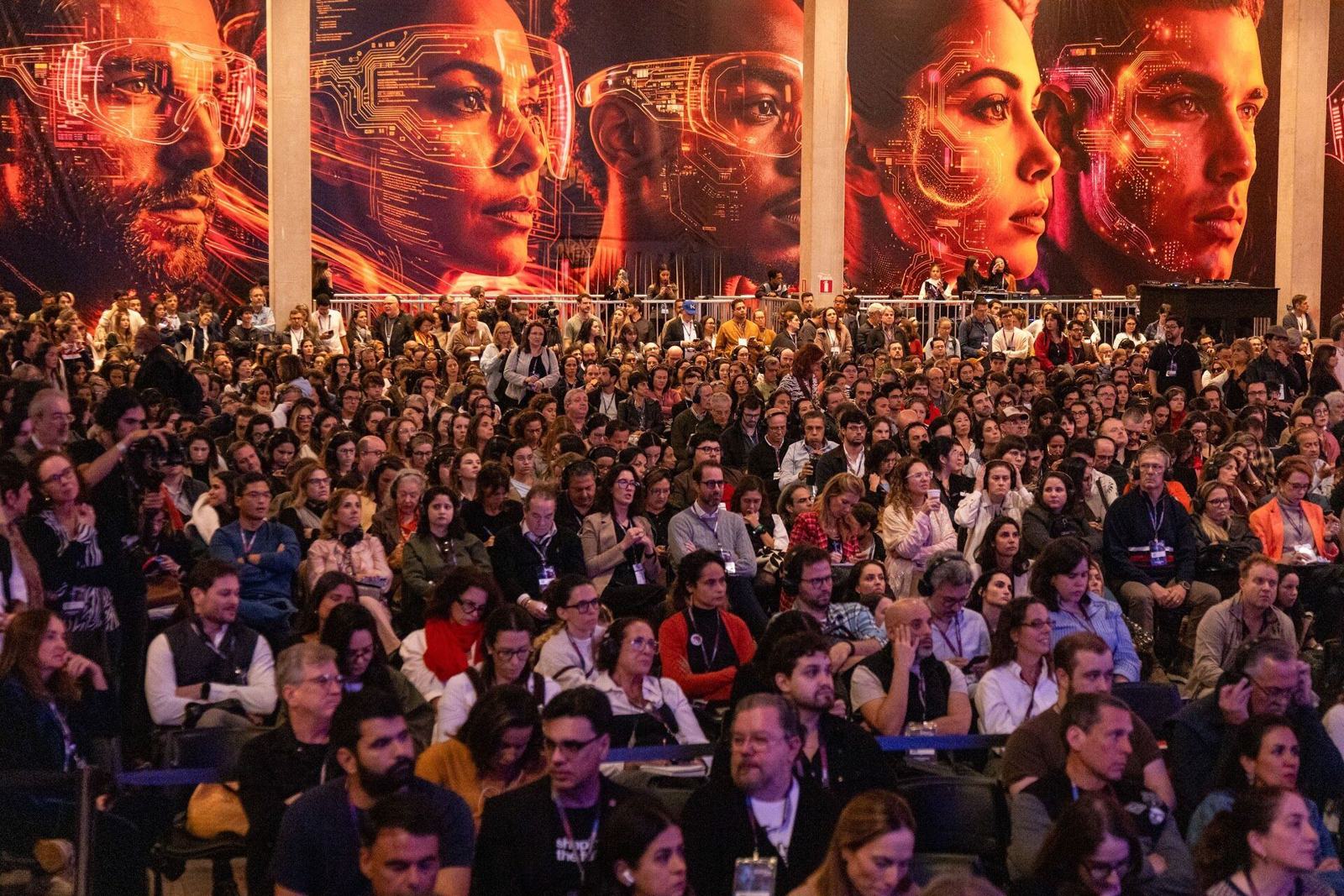 Packed audience in front of an LED wall showing faces